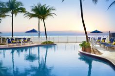 an outdoor swimming pool with lounge chairs and umbrellas next to the ocean at sunset