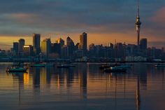 the city skyline is reflected in the calm water at sunset, with sailboats floating on the bay