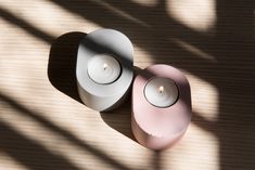 two white and pink candles sitting next to each other on a wooden surface with shadows