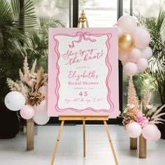 a pink and white sign sitting on top of a wooden easer next to balloons