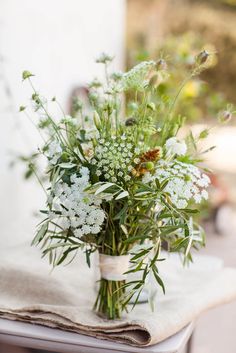 a vase filled with lots of white flowers on top of a wooden table next to a napkin