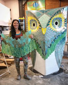 a woman standing next to an owl statue made out of stained glass and paper machs