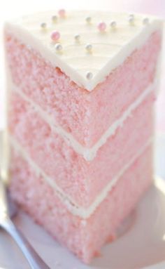 a piece of pink cake sitting on top of a white plate next to a fork