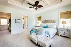 a bedroom with white walls and carpeted flooring has a large bed, two nightstands, and a ceiling fan