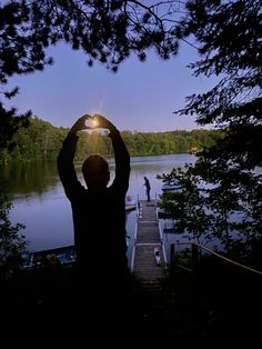 a man is holding his hands up in the air while standing on a dock at night