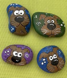 four painted rocks with dogs on them sitting next to each other in front of a green background