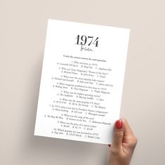 a person holding up a sheet of paper with the year 1974 written on it