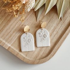 a pair of white earrings sitting on top of a wooden tray next to a plant