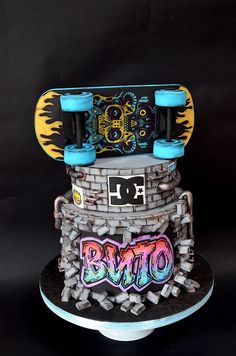 a skateboard cake is decorated with graffiti on the top and bottom tier, as well as an image of a brick wall