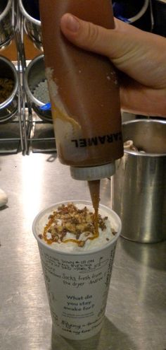 someone is pouring something into a cup with ice cream on it and toppings in the background