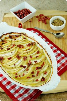 a baked dish with potatoes and bacon on a wooden cutting board