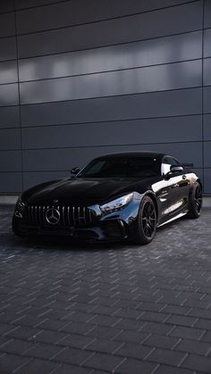 a black mercedes sports car parked in front of a building with its hood up and lights on