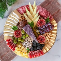 an assortment of cheeses, meats and grapes on a platter with pine cones