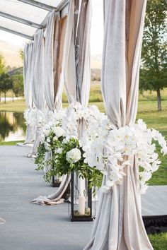 white flowers in vases are lined up on the side of a building with drapes