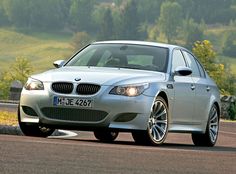 a silver car driving down a road next to a lush green hillside with trees in the background