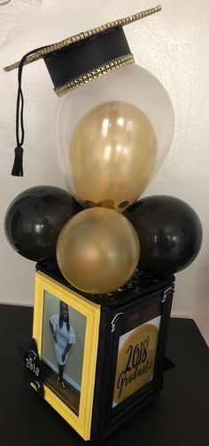 a graduation cap and balloons on top of a small box with a photo in it