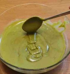 a wooden spoon in a glass bowl filled with green liquid on top of a table