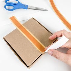 someone is cutting out some brown tape on top of a piece of cardboard with scissors