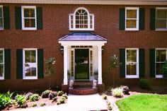 a red brick house with white trim and green shutters on the front door is shown