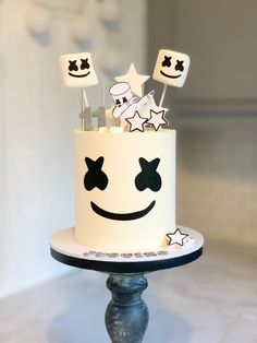 a white cake decorated with smiley faces and stars on a stand in front of a wall