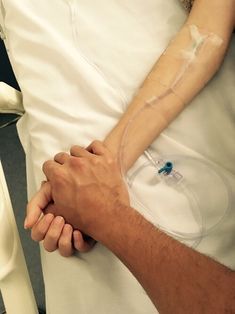 a man holding the hand of a woman in a hospital bed with an iv drip attached to his arm