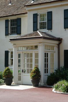 a white house with black shutters and two large potted plants