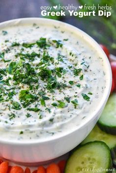 a white bowl filled with greek yogurt dip surrounded by cucumbers and carrots