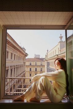 a woman sitting on a window sill looking out