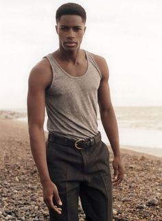 a man standing on top of a rocky beach next to the ocean with his hands in his pockets