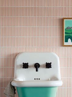 a bathroom sink with two faucets on the wall and a painting above it