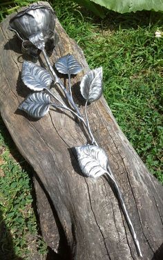 two metal flowers sitting on top of a piece of wood in the grass next to a leafy plant