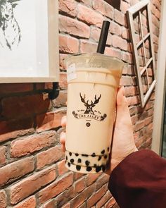 a person holding up a drink in front of a brick wall with an antler on it