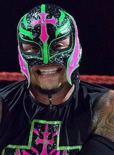 a man wearing a neon green and pink wrestling mask with cross on it's chest