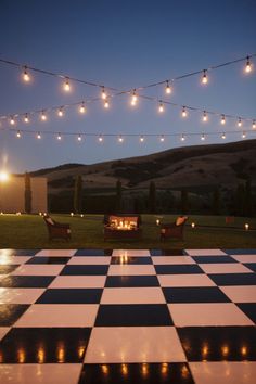 a checkerboard dance floor is lit up at night with fairy lights strung over it