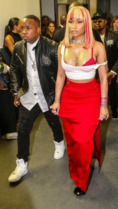 a woman in a red and white dress walking next to a man wearing a black leather jacket