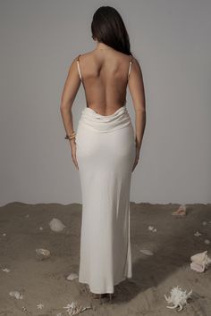 a woman in a white dress is standing on the beach with her back to the camera