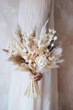 a woman in a white dress holding a bouquet of dried flowers and grasses with her hands