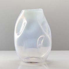 a glass vase sitting on top of a white table next to a gray wall in the background