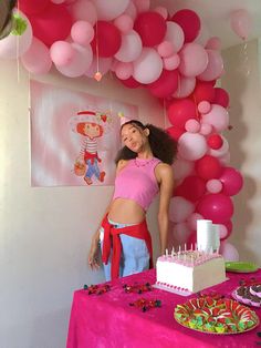 a woman standing next to a table with cake and balloons