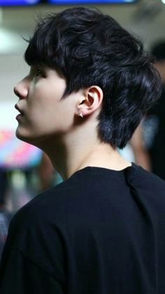 a young man with black hair and piercings on his ears looking off into the distance