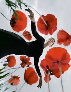 a woman standing among red flowers with her arms in the air, looking up into the sky