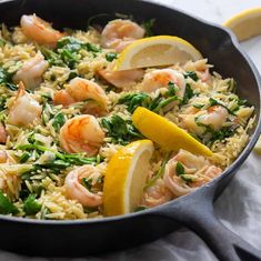 a skillet filled with shrimp, rice and spinach on top of a table