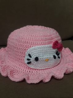 a crocheted hello kitty hat with a bow on the brim, sitting on a couch