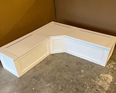 a white corner bench sitting on top of a cement floor next to a brown wall