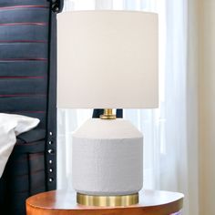 a white lamp sitting on top of a table next to a night stand with a bed in the background