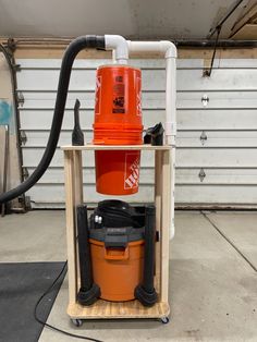 an orange bucket sitting on top of a wooden stand next to a black and white hose