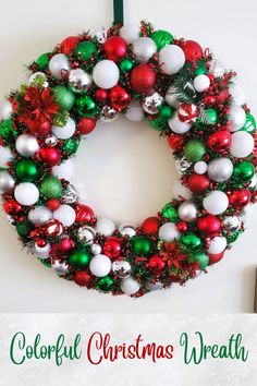 a colorful christmas wreath with ornaments hanging on the front door and text overlay that reads colorful christmas wreath