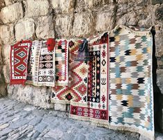 several colorful rugs hanging on a stone wall