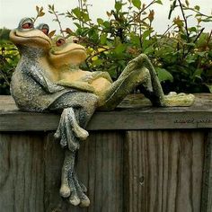 a statue of two frogs sitting on top of a wooden fence