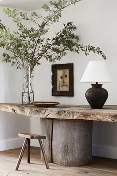 a wooden table topped with a vase filled with green leaves next to a tree branch